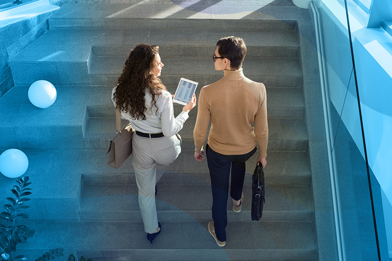 Two coworkers walking up a staircase sharing something on an ipad