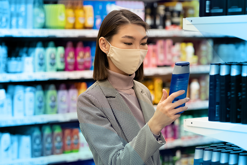 young woman looking at hair care product in grocery store setting