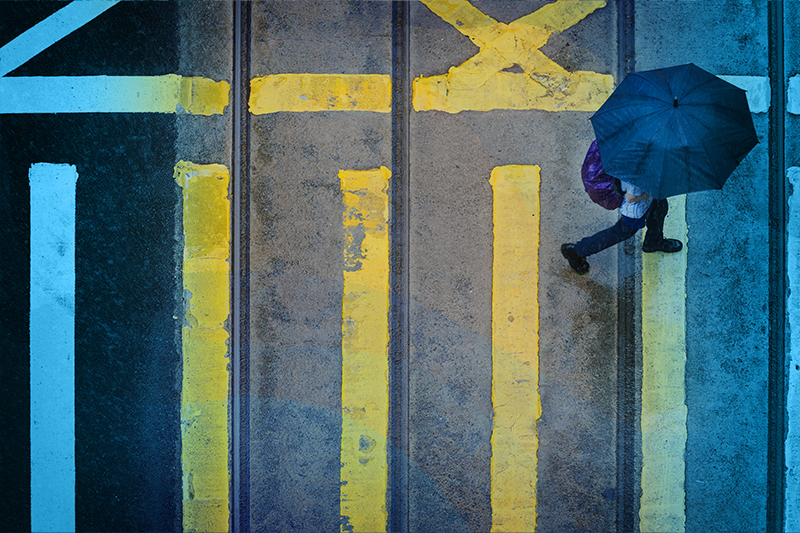 photo of person holding umbrella while walking across crosswalk in Hong Kong