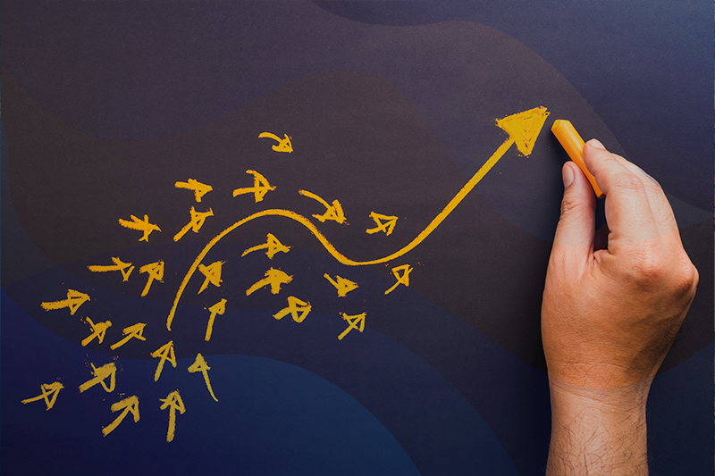 photo of a hand drawing an upward moving arrow on a chalkboard