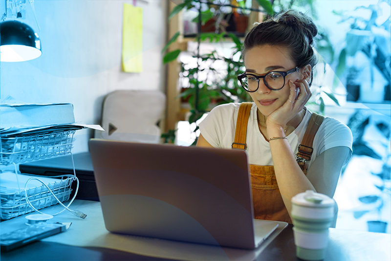 a young woman in glasses works on a laptop in her home