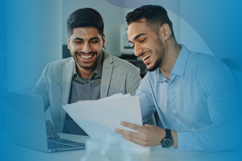 Two men reviewing paperwork together at a desk with a laptop in front of them