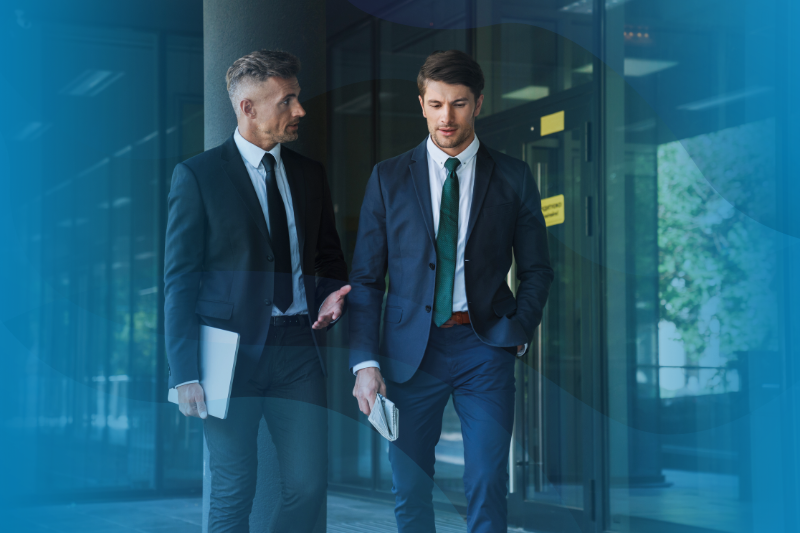 Two businessmen dressed in formal suits walking and having a conversation outside of WilsonHCG's office building.