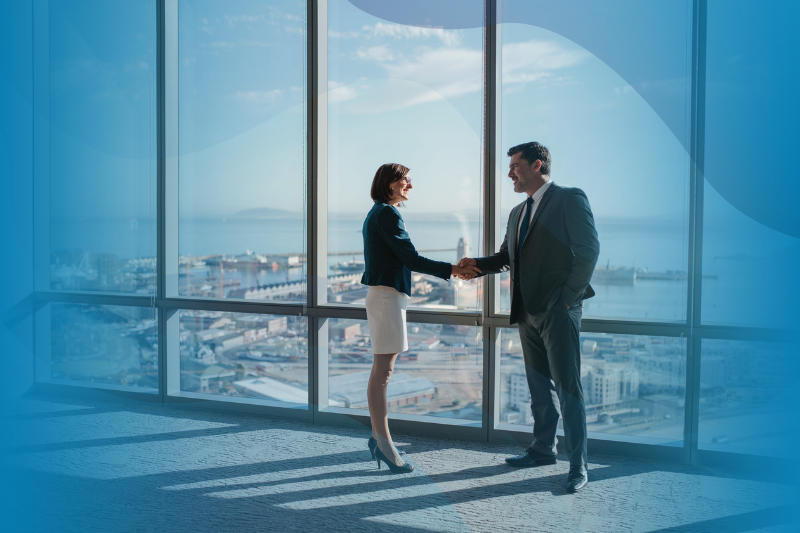 Businessman and businesswoman shaking hands together while standing in front of WilsonHCG office building windows overlooking the city