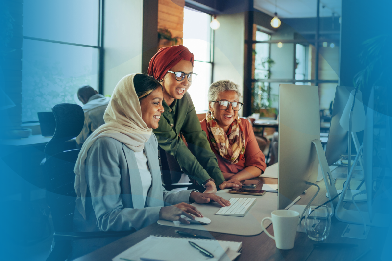 Three female employees at WilsonHCG look at a computer screen.