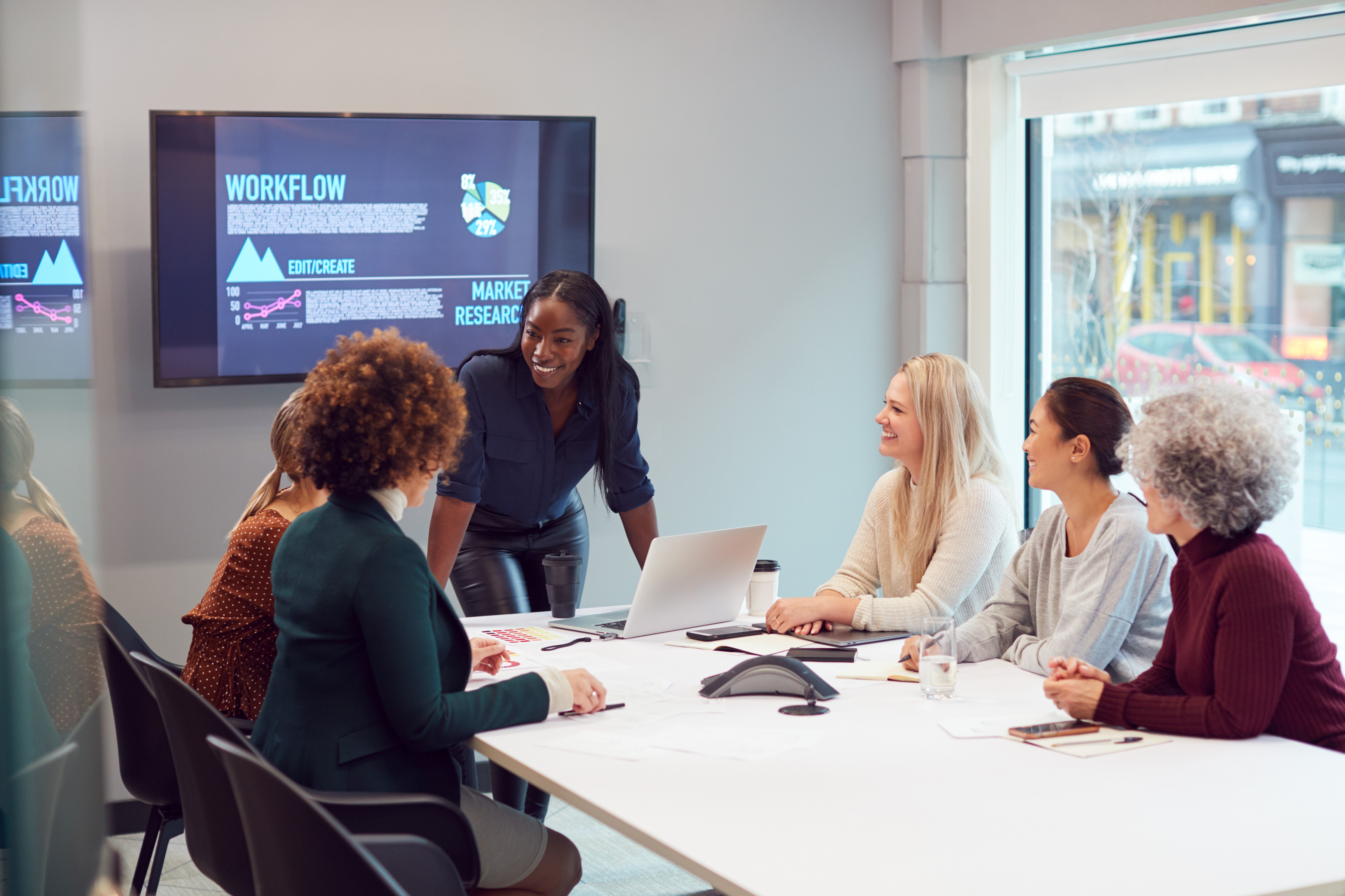 Young Businesswoman Leading Meeting Of Women Collaborating Around Table In Modern Office Young Businesswoman Leading Meeting Of Women Collaborating Around Table In Modern Office