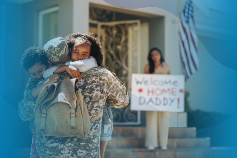 Military Dad Hugging His Children After Returning Home in Foreground. Military Wife Holding a Welcome Home Sign in Background.