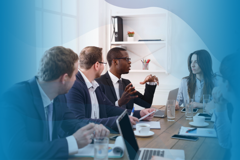 Group of men and women around a conference table with a man talking