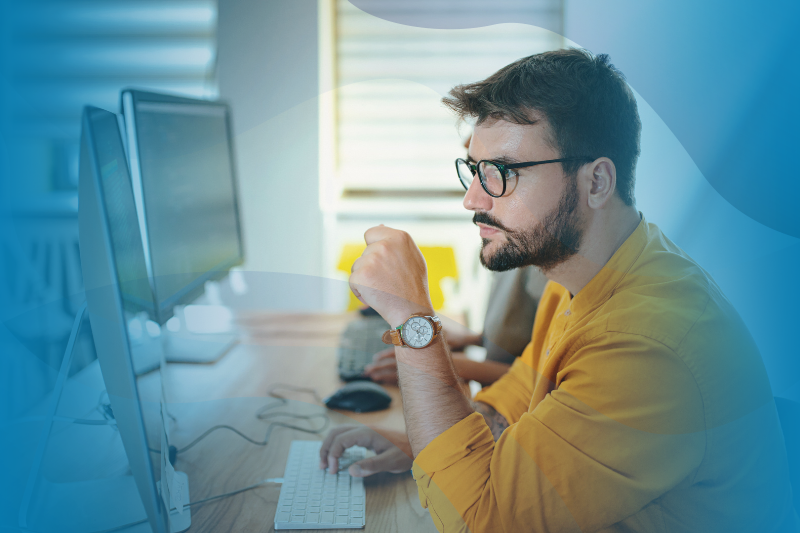 Man in a yellow shirt on a dual-screen computer home office setup at home